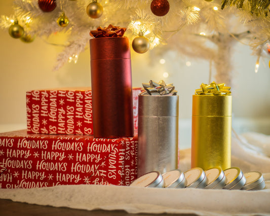 A set of six decorative mini candles in red, yellow, and silver colors, placed in a festive holiday setting with Christmas decorations around.